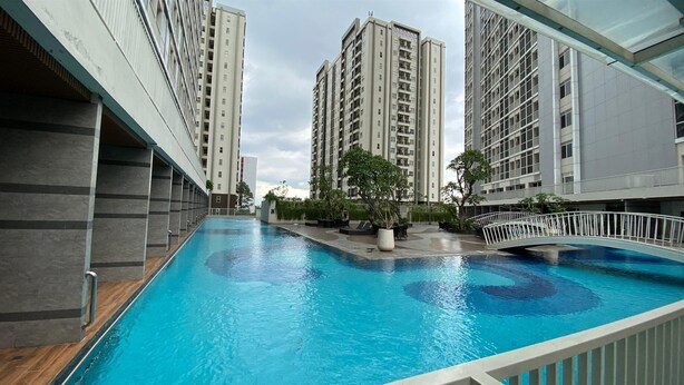 A swimming pool area with modern buildings in the background. - Good Studio Near Binus At Pacific Garden Apartment (Tangerang)