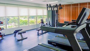 A gym with exercise equipment, large windows, and a view of greenery. - Good Studio Near Binus At Pacific Garden Apartment (Tangerang)