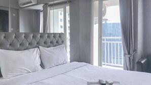 A hotel room with a large bed, a headboard, a window with curtains, an air conditioning unit, and a remote control on a bedside table. - Good Concept Studio At Tanglin Supermall Mansion Apartment (Surabaya)