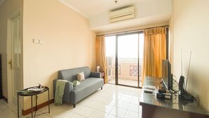 A living room with a sofa, a glass table, a TV, and a balcony with curtains. - Spacious And Comfy 3Br At Puri Garden Apartment (Jakarta)