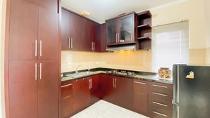 A kitchen with dark brown cabinets, a stainless steel sink, and a black refrigerator. - Spacious And Comfy 3Br At Puri Garden Apartment (Jakarta)