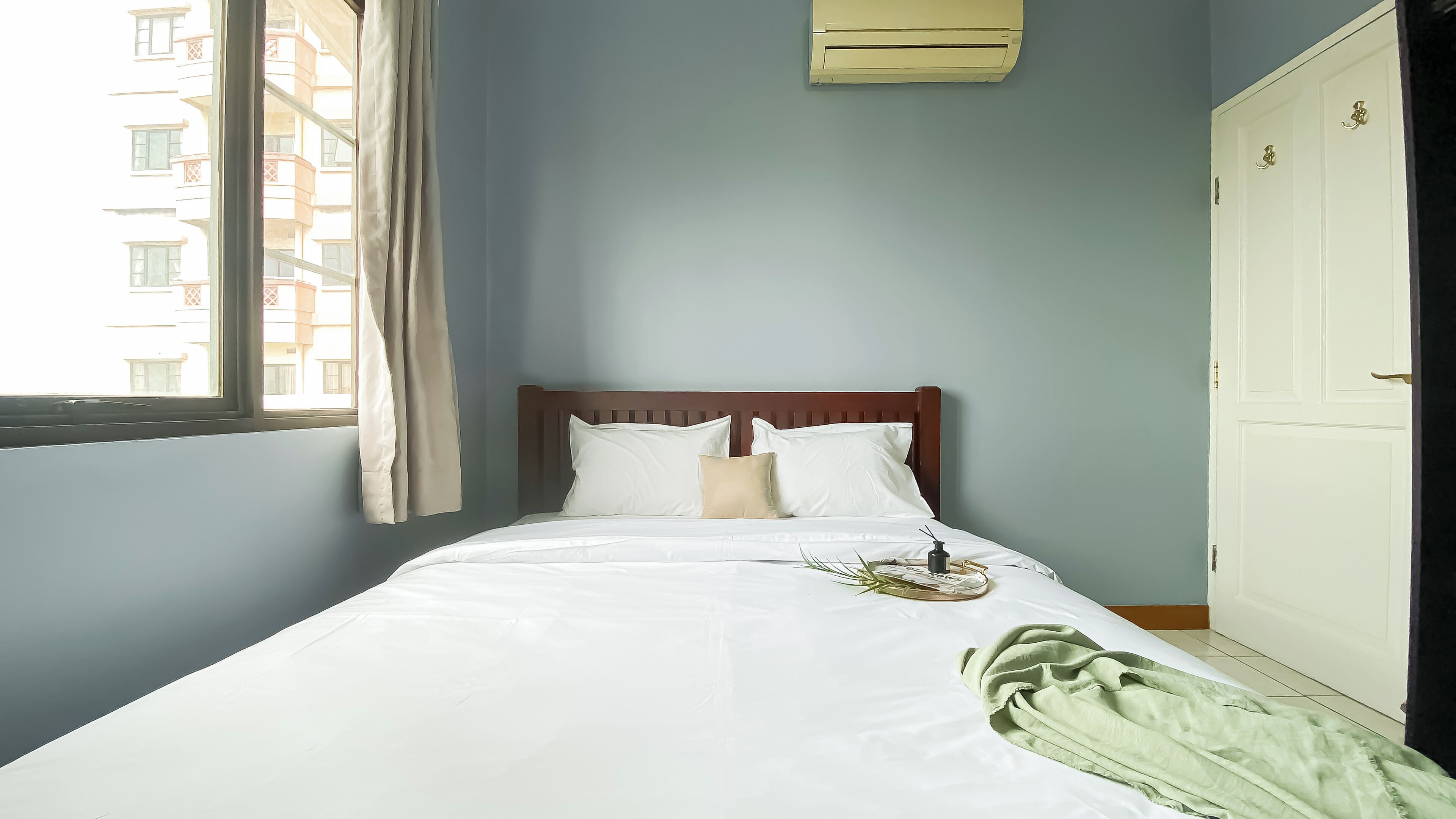 A neatly made bed with white linens, a wooden headboard, and a green throw blanket.