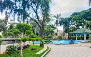 Un área ajardinada con piscina, rodeada de árboles y un pabellón.
