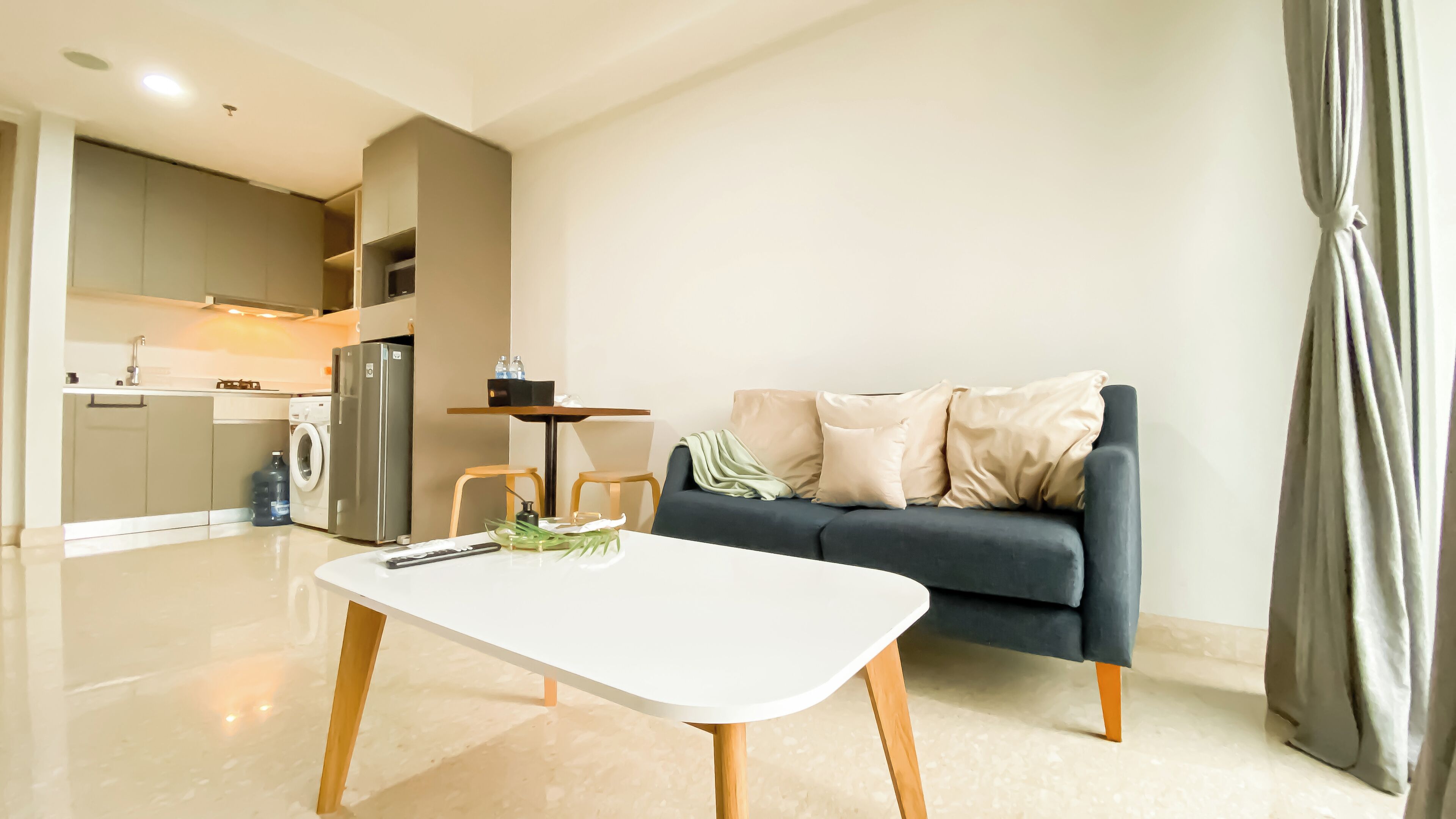 A modern living room with a dark blue sofa, a white coffee table, and a kitchen area in the background.