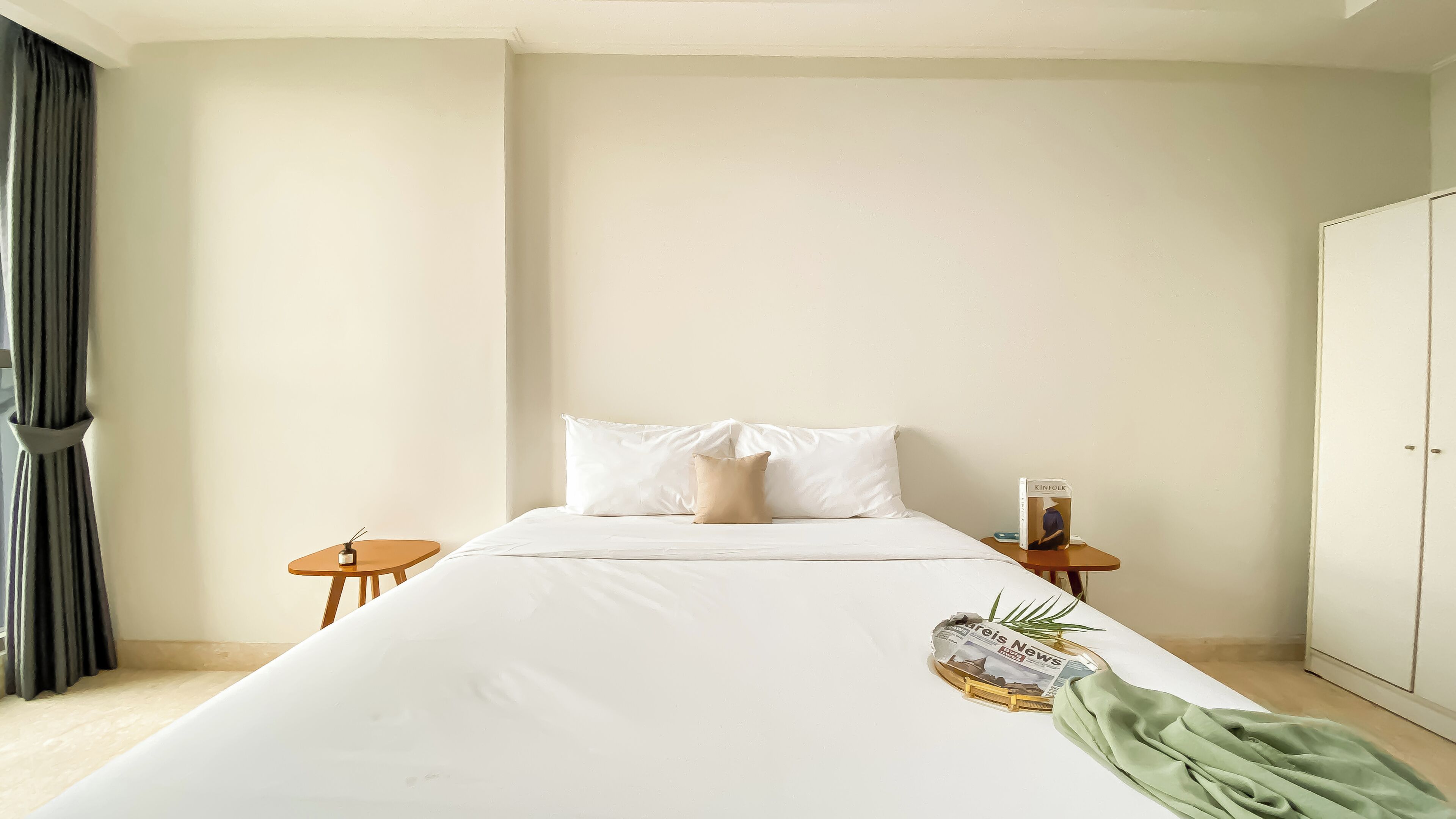 Een minimalistisch hotelkamer met een groot bed, een klein nachtkastje, een bijzetmeubel en een garderobe.