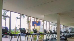 A gym with treadmills and exercise bikes, large windows, and a TV screen.