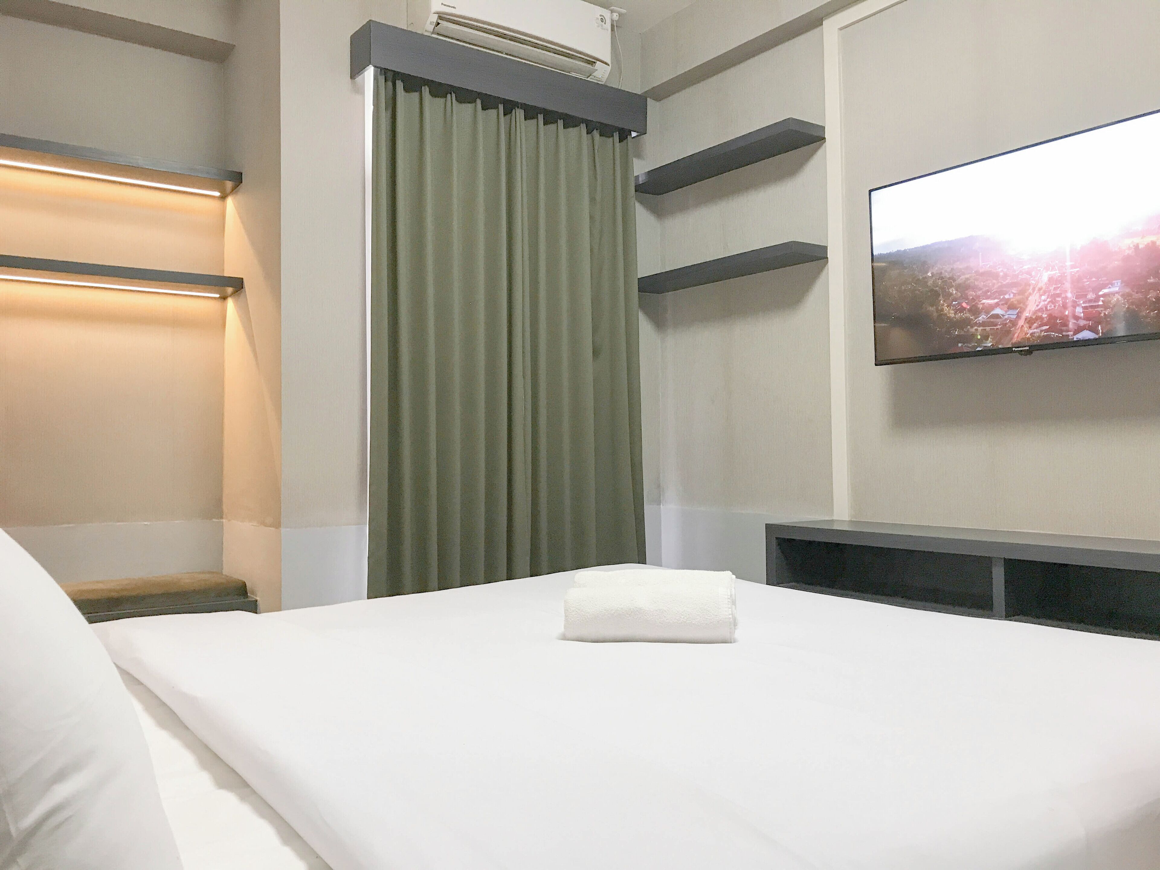 A hotel room with a bed, a television mounted on the wall, and a window with curtains.
