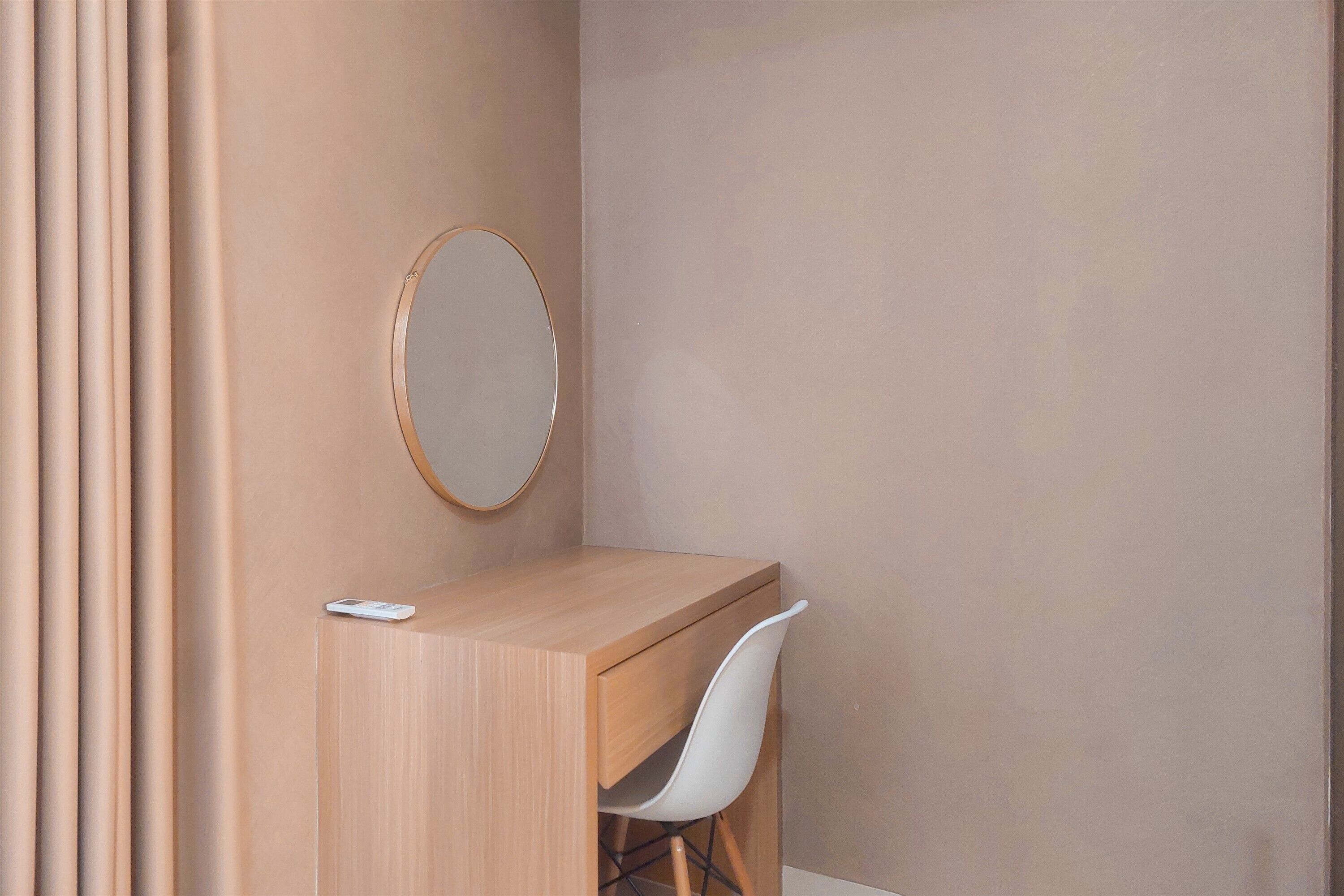 Une petite pièce moderne, avec un bureau en bois, une chaise blanche et un miroir rond accroché au mur.