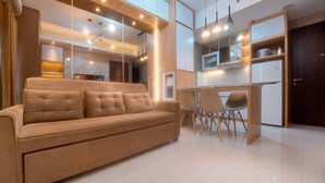 A modern living room with a beige sofa, a dining area with a table and chairs, and a kitchen in the background. - Cozy And Elegant 2Br Apartment At Transpark Bintaro (South Tangerang)