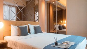 A hotel room with a large bed, a bedside table, a nightstand, and a mirror. - Cozy And Elegant 2Br Apartment At Transpark Bintaro (South Tangerang)