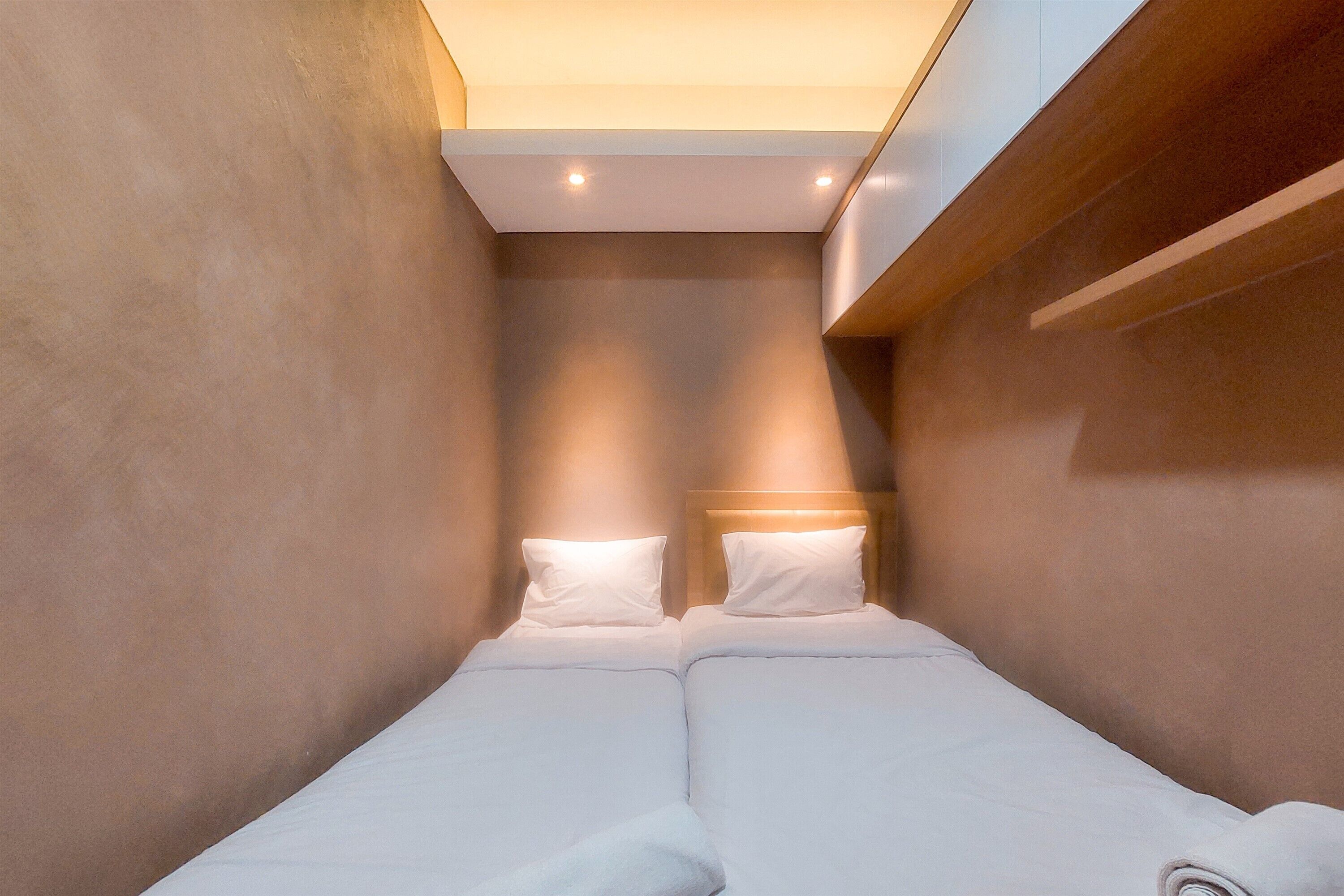 A compact, modern room with two single beds, a wooden headboard, and recessed ceiling lighting.