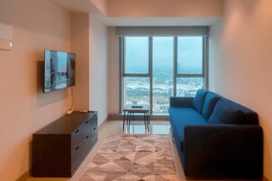 A modern living room with a large window, a flat-screen TV, a dark blue sofa, and a patterned rug.