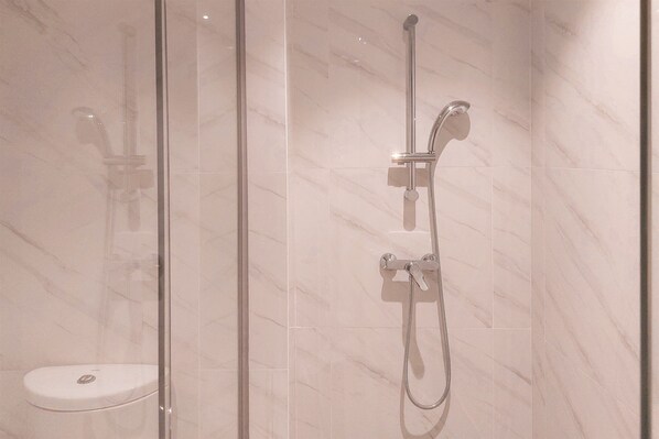 A glass-enclosed shower with a handheld showerhead and a fixed overhead faucet.