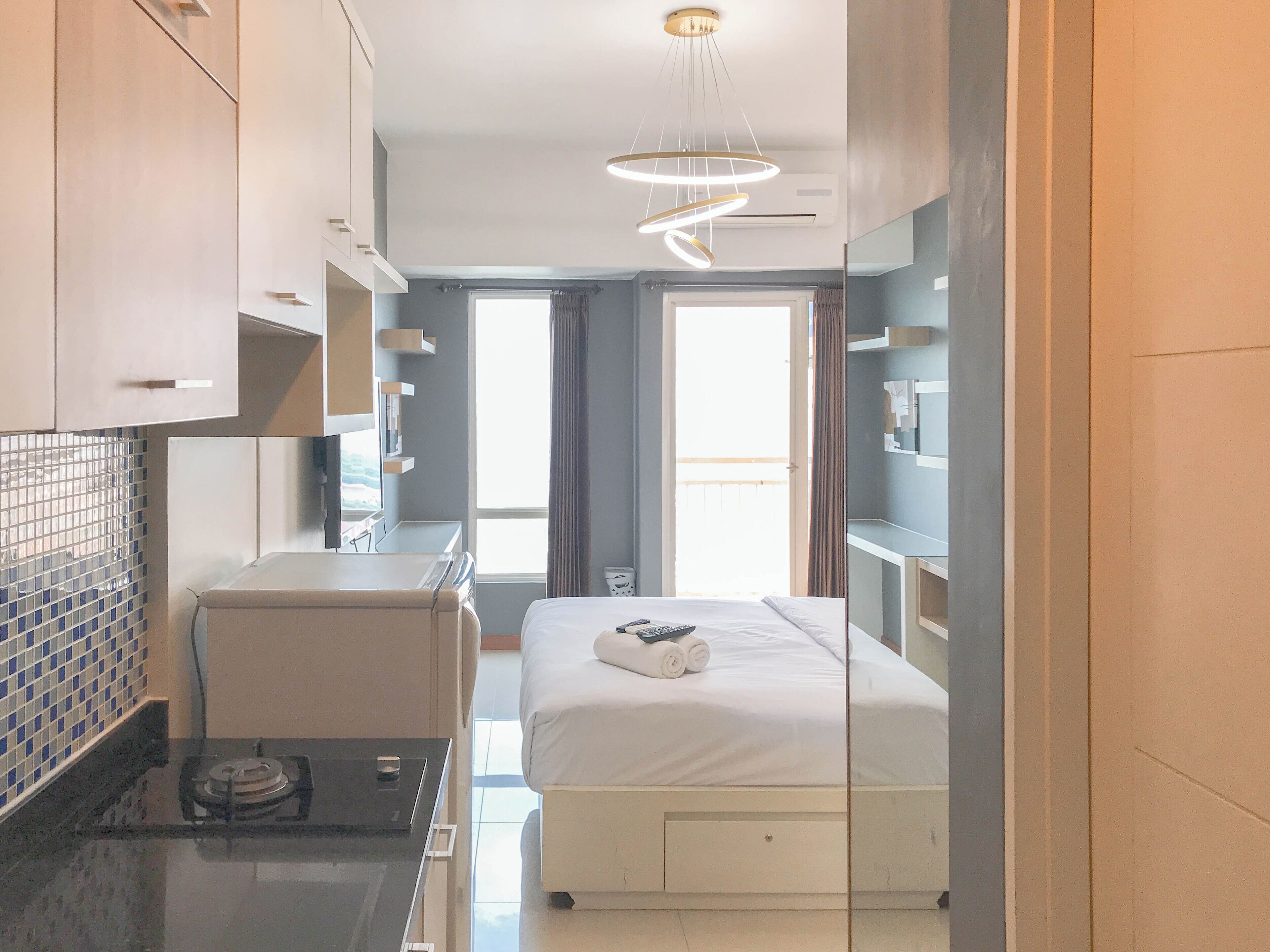 A modern hotel room with a bed, a small desk, a mirror, and a window with curtains.