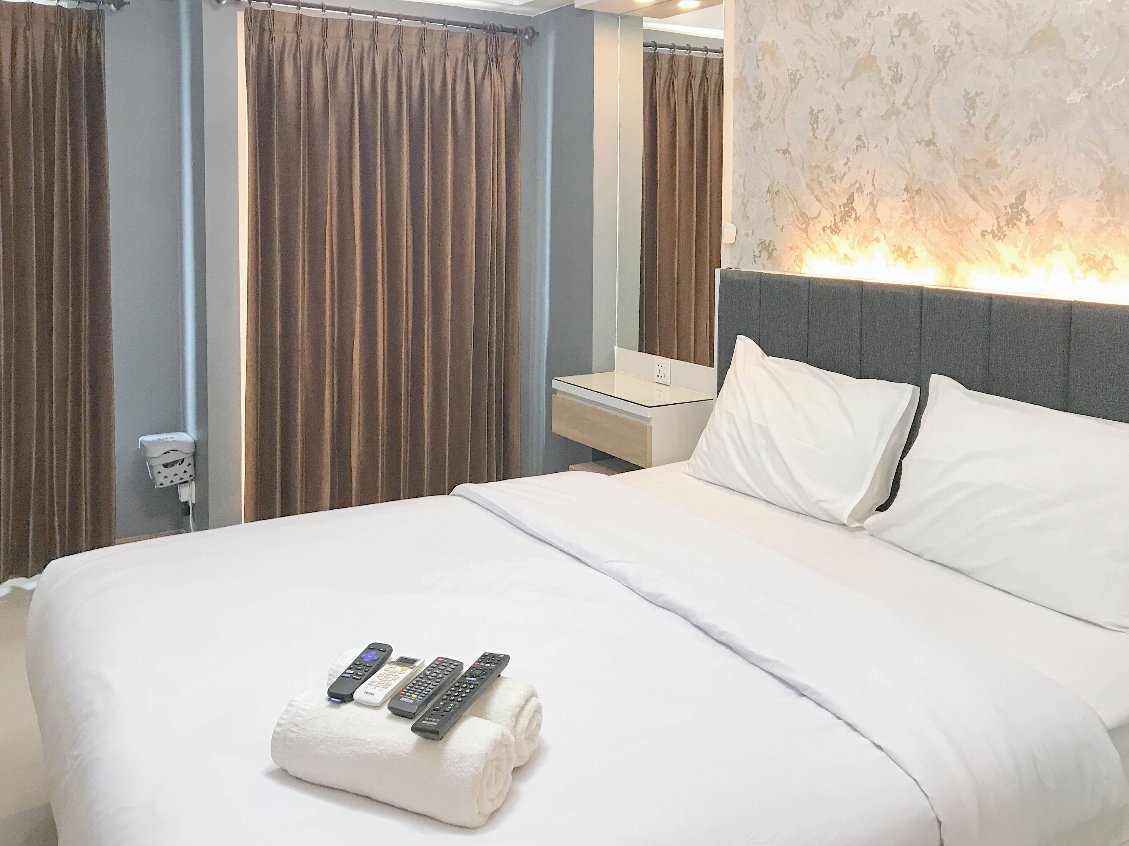 Une chambre d’hôtel avec un lit bien fait, une table de chevet, un miroir et un luminaire fixé au mur.