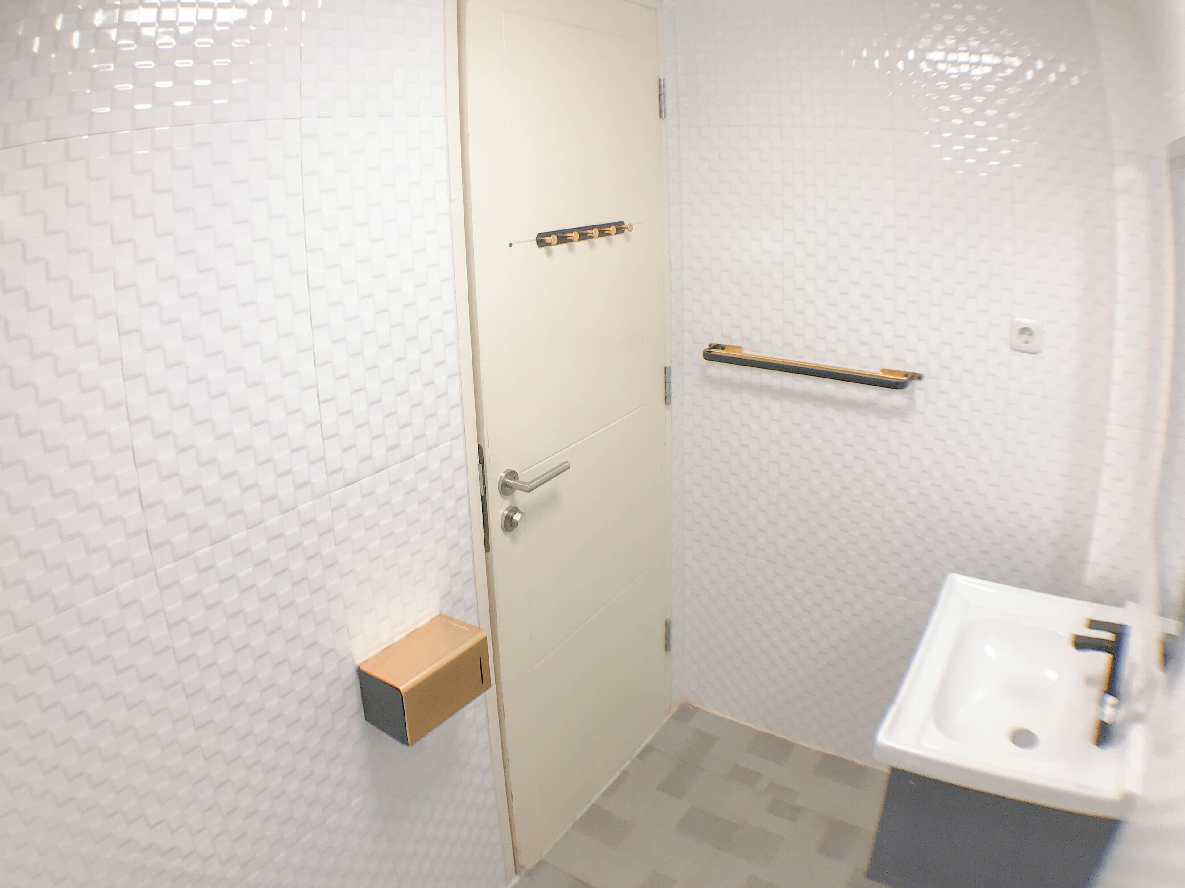 A bathroom with a white tiled wall, a door with a handle, a towel rack, and a sink with a faucet.