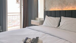 Habitación de hotel con una cama grande, una mesita de noche, un espejo y vistas a la ciudad desde la ventana.