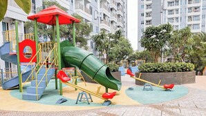 Un patio de juegos con un tobogán verde, columpios y un sube y baja.