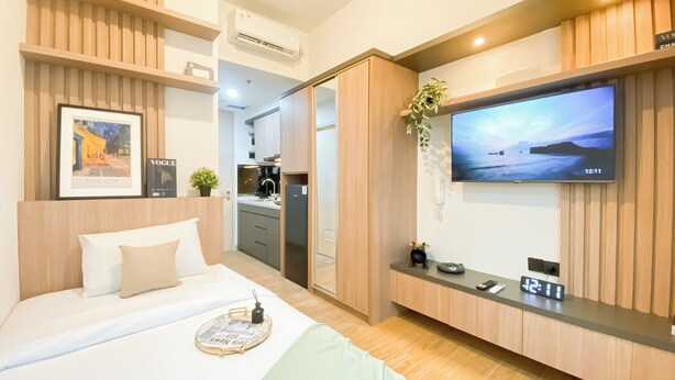 Une chambre d’hôtel moderne équipée d’un lit, d’un téléviseur fixé au mur, d’un petit coin cuisine et d’une tête de lit en bois.