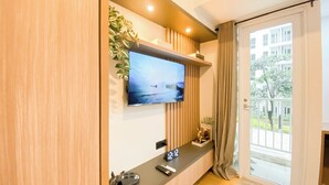 Une chambre d’hôtel moderne équipée d’un téléviseur à écran plat fixé au mur, d’une petite table avec une horloge, des télécommandes et un objet décoratif.
