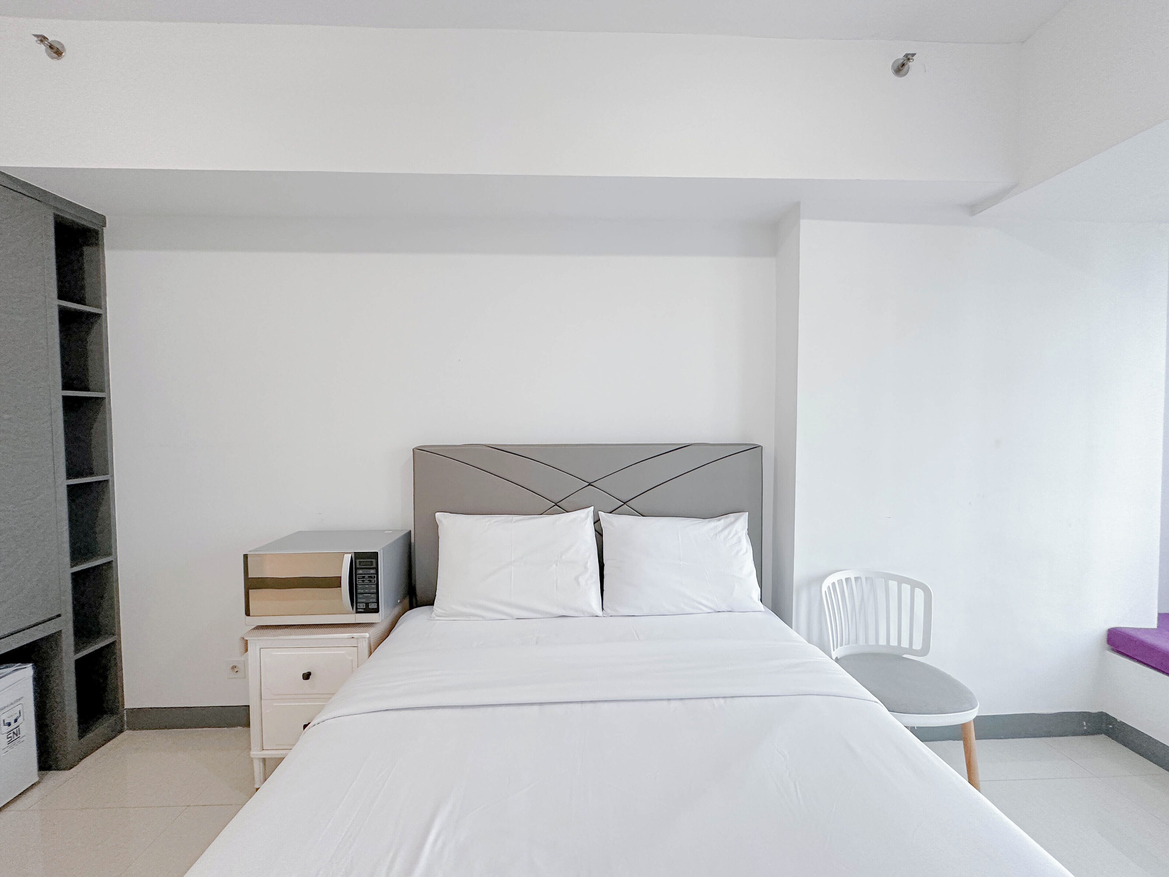 A bedroom with a bed, a nightstand, a chair, and a shelving unit.