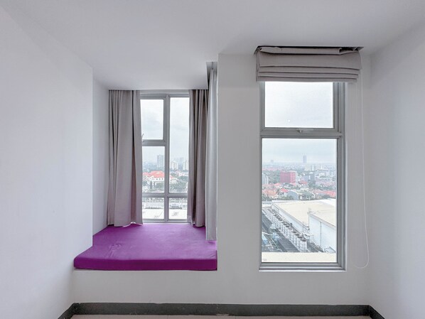 Une pièce dotée d’une grande fenêtre, d’un banc rembourré de coussins violets et offrant une vue sur le paysage urbain.