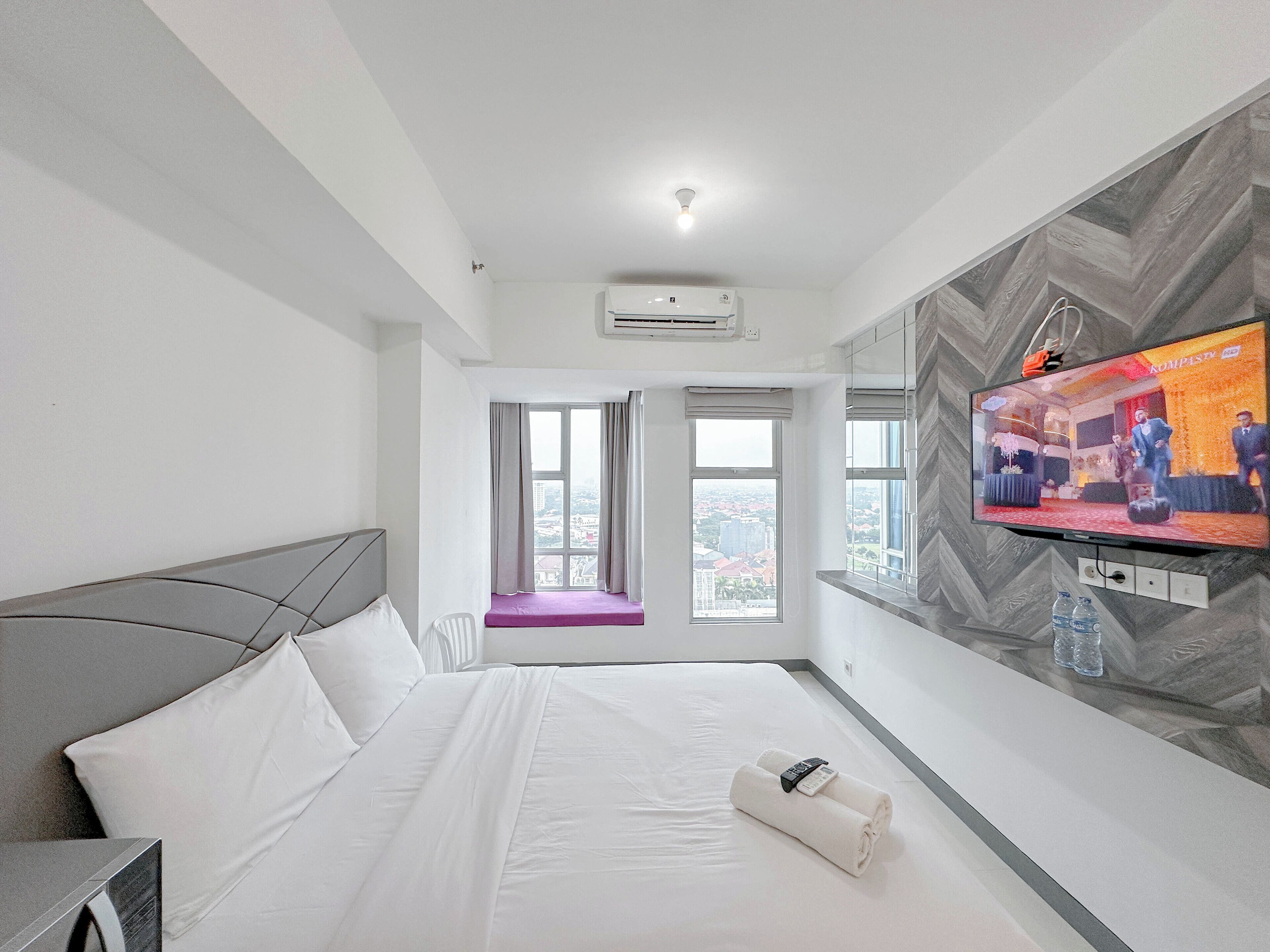 A hotel room with a bed, a TV, and a window with a view of buildings.