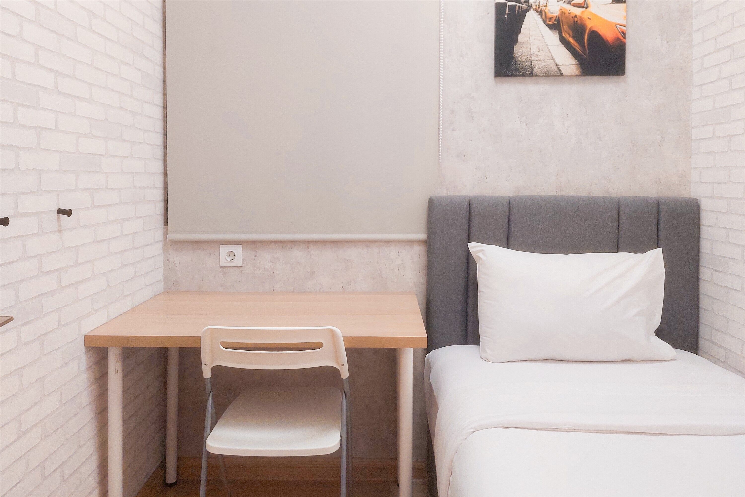 A small room with a bed, a desk, and a chair. There is a picture on the wall.