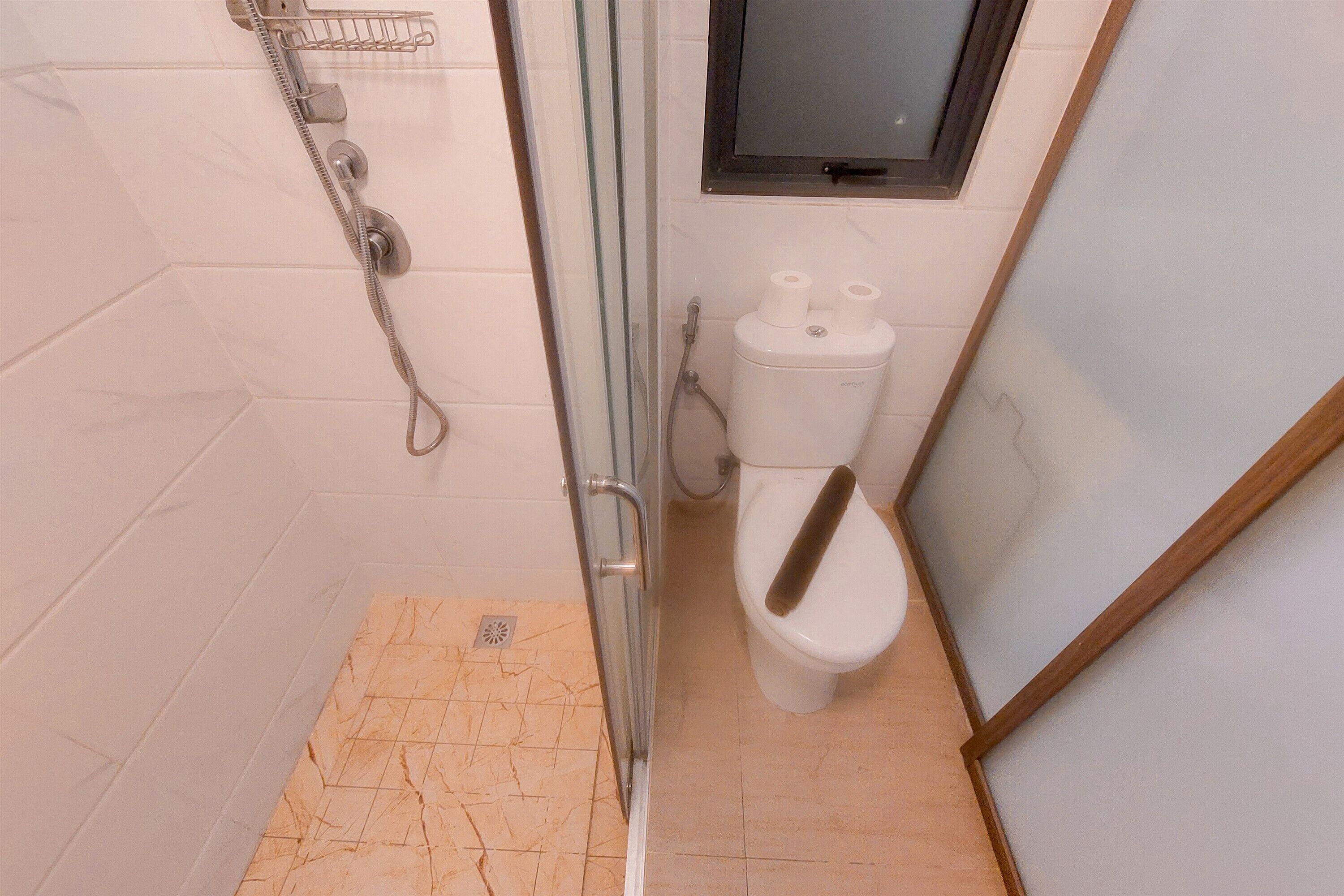Ein Badezimmer mit Duschkabine aus Glas, Toilette und kleinem Fenster über der Toilette.