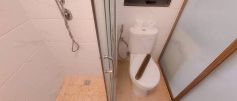 Ein Badezimmer mit Duschkabine aus Glas, Toilette und kleinem Fenster über der Toilette.