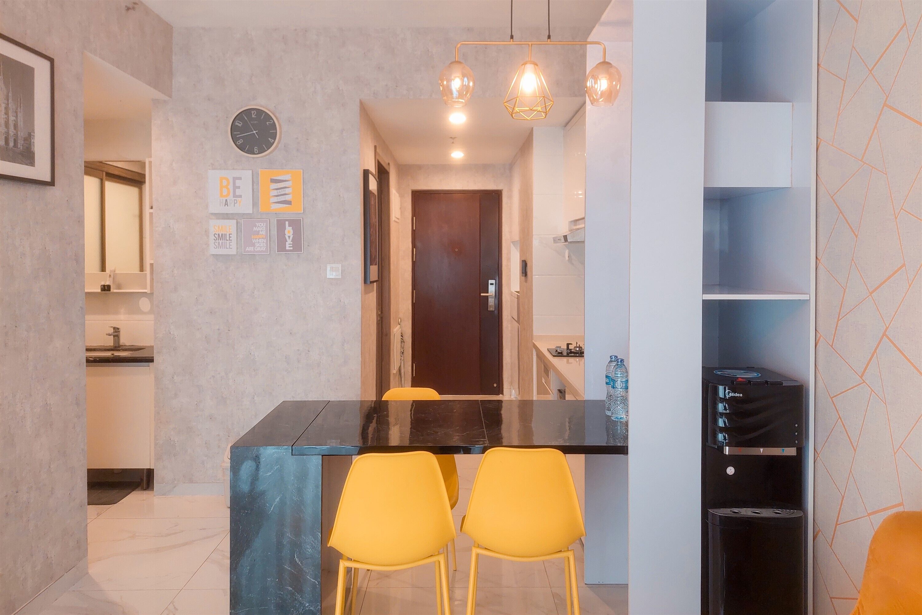 A modern kitchen with a black countertop, yellow chairs, and a water dispenser.