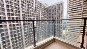 Un balcón con barandilla de cristal, con vistas a un edificio residencial alto.