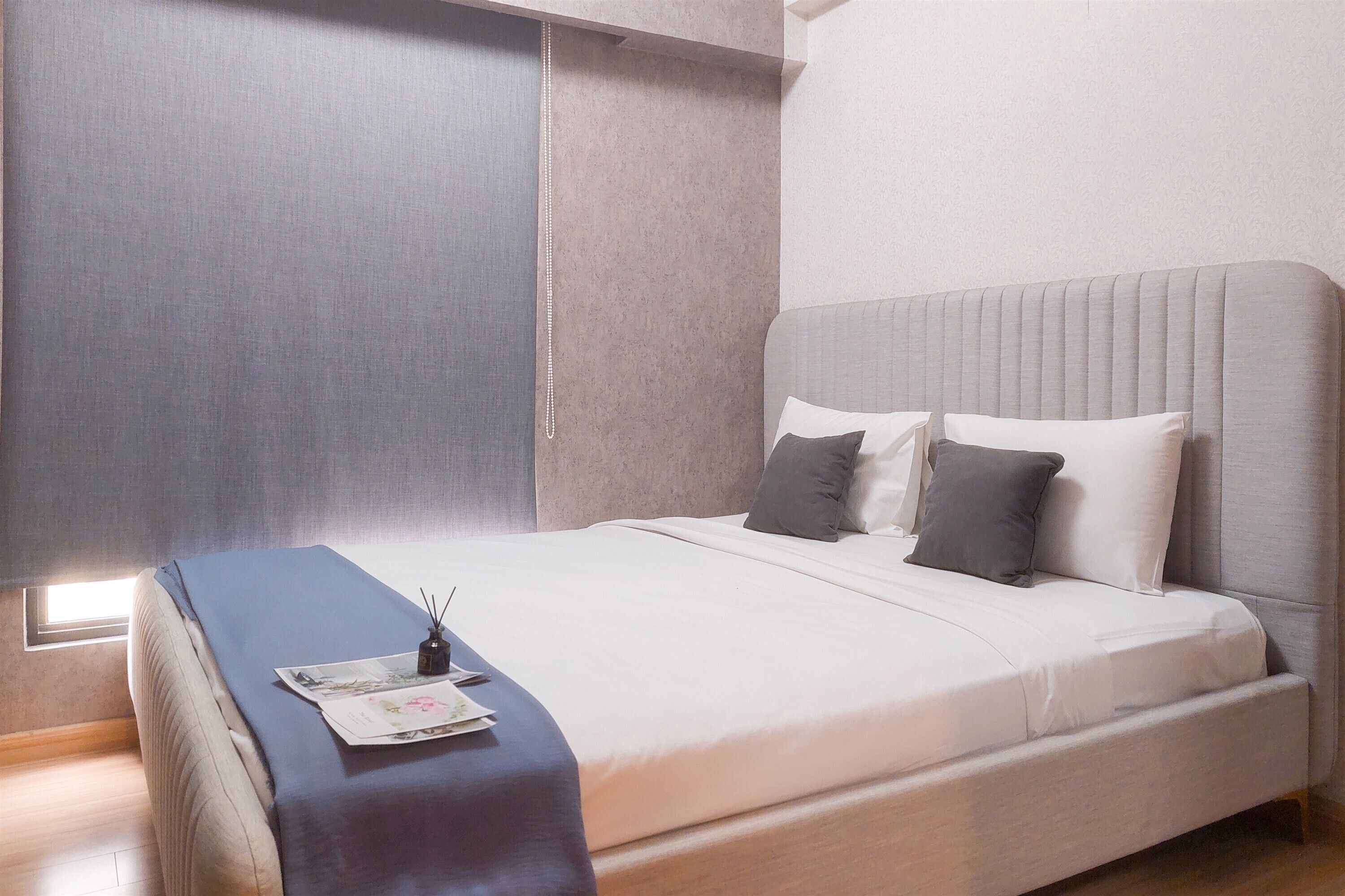 A modern bedroom with a large bed, a bedside table with a lamp, and a window providing natural light.