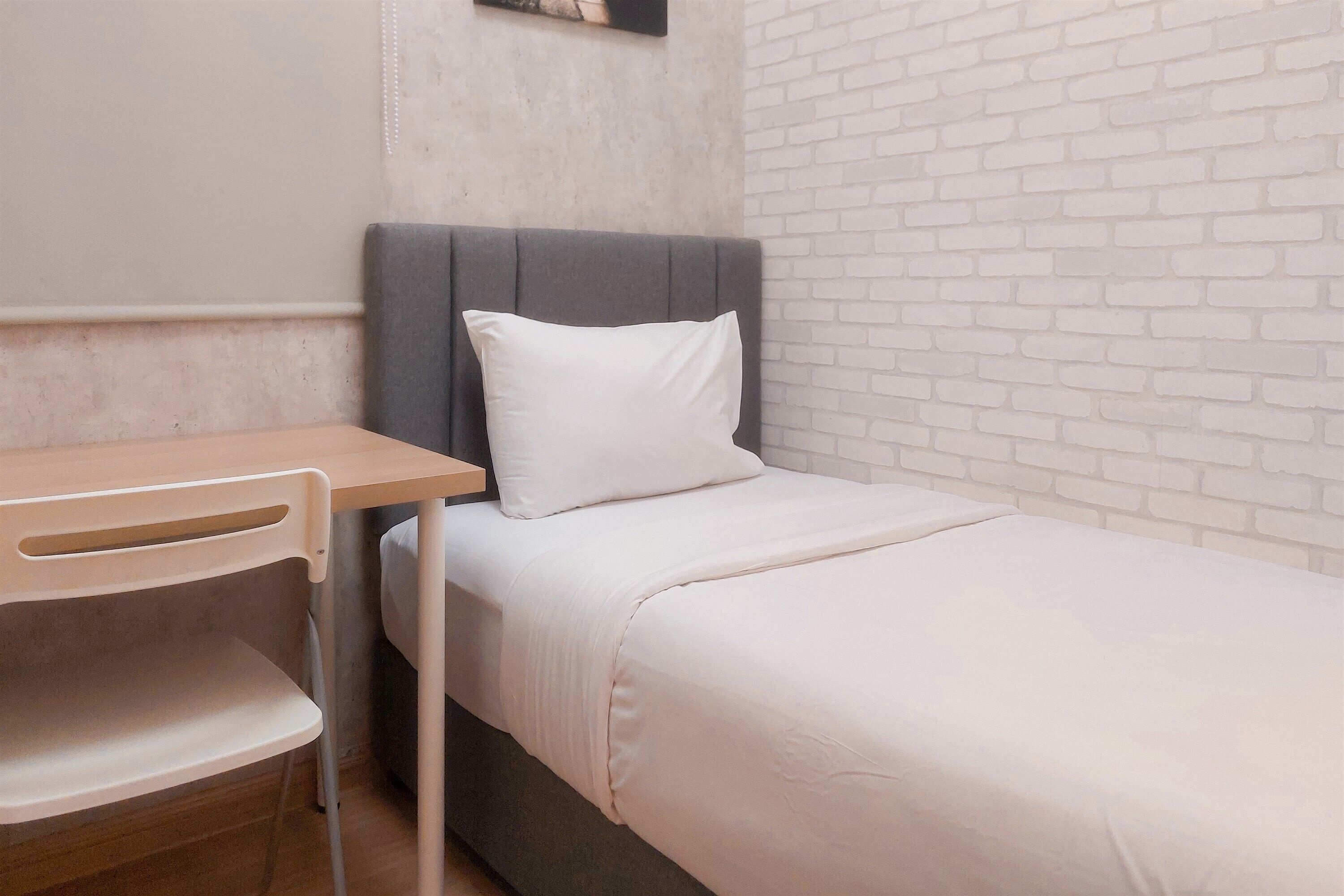 Un dormitorio pequeño y ordenado con una cama individual, una mesita de noche y una silla.
