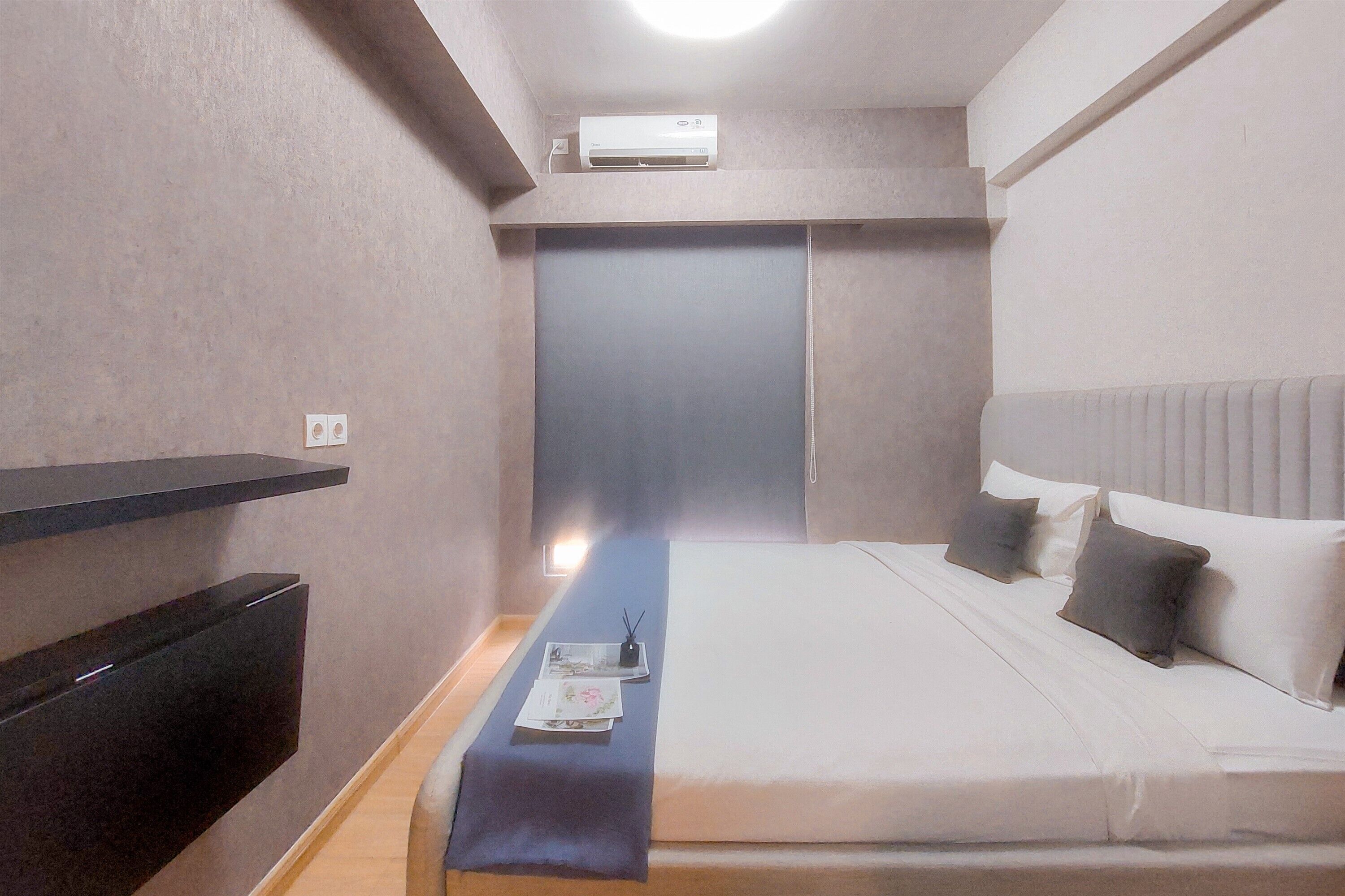 A hotel room with a bed, bedside table, and a wall-mounted air conditioner.