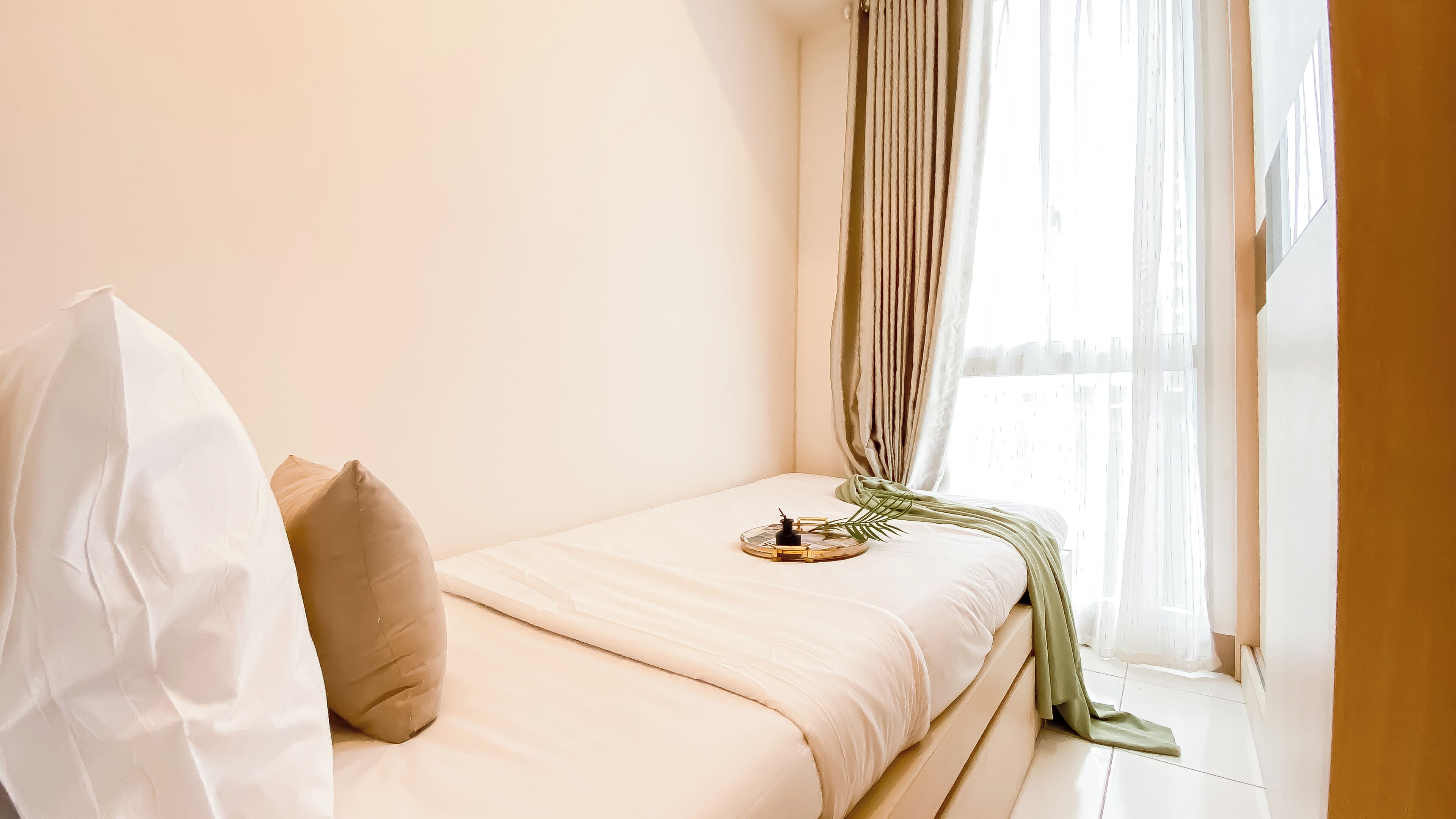 A small, neatly made bed with a white and beige color scheme, a green throw blanket, and a small decorative item on the bed.