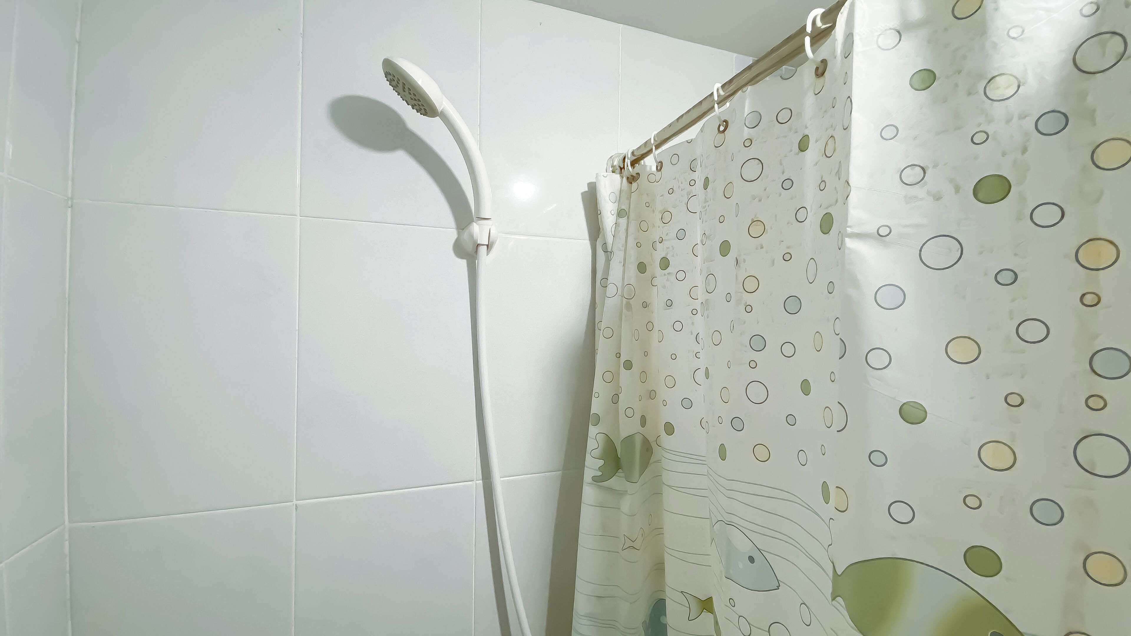 Zona de ducha con pared de azulejos blancos, cabezal de ducha y cortina con estampado de lunares.