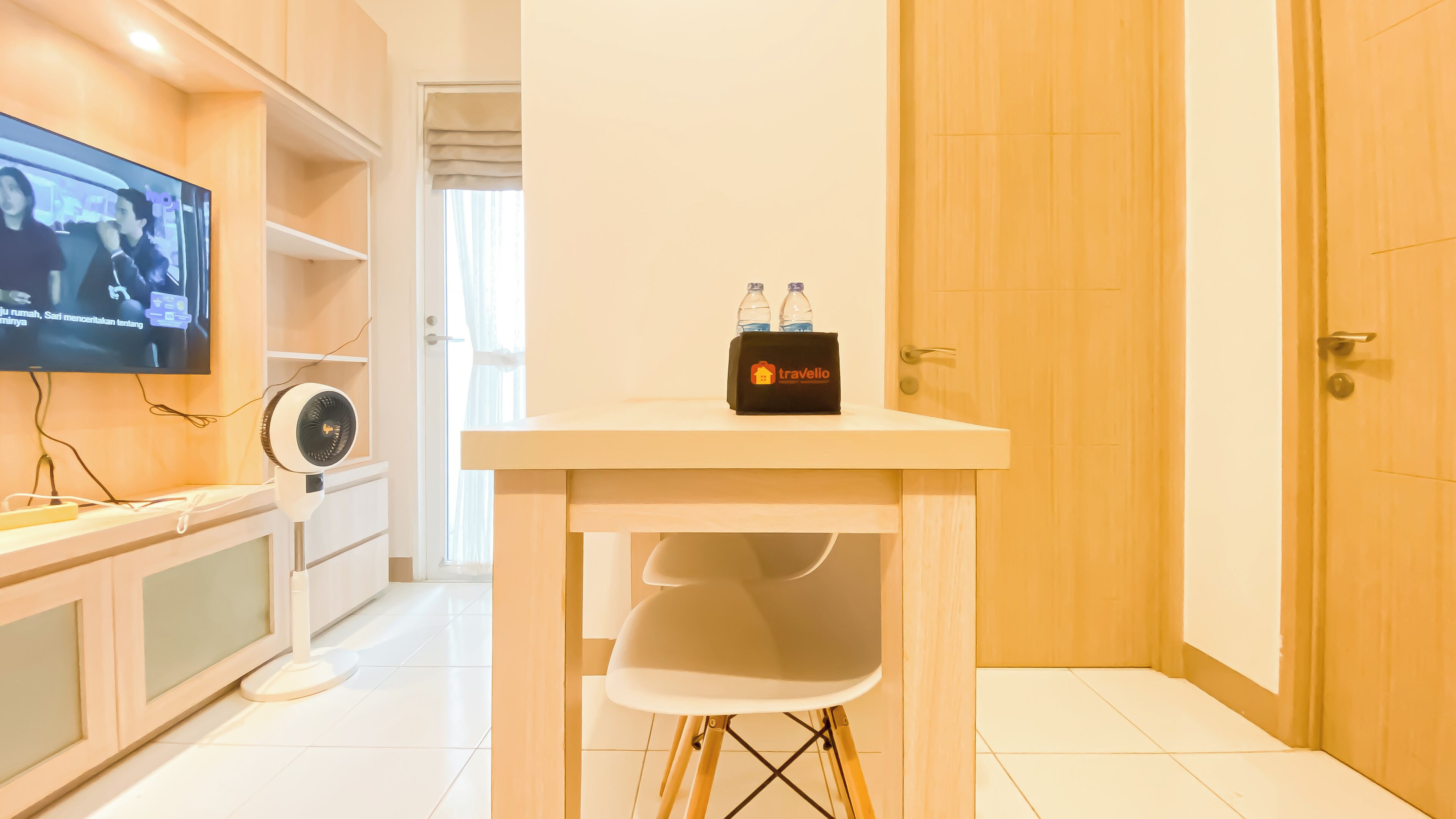 A hotel room with a television, a small table with a bottle holder, and a door.