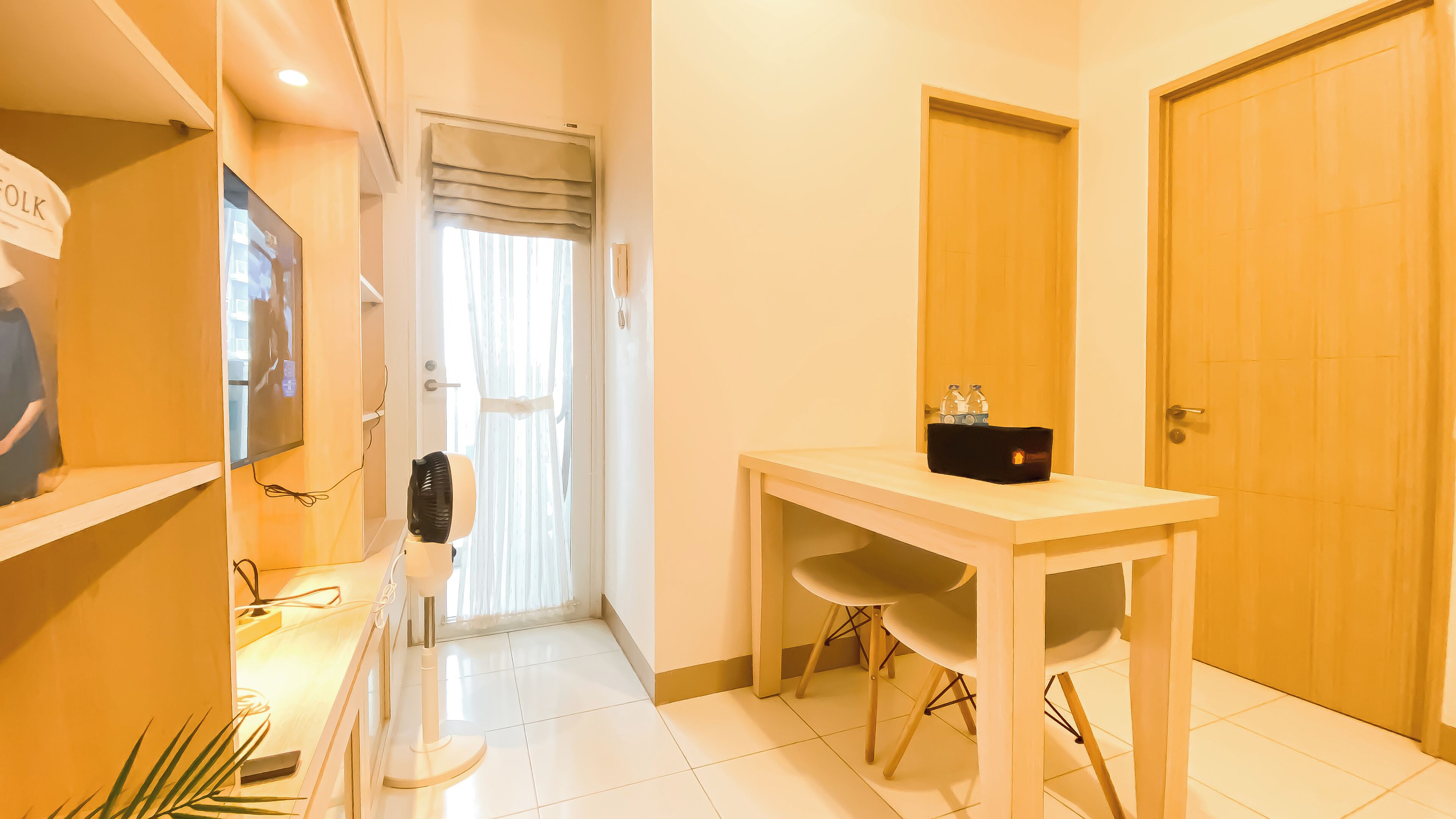 A hotel room with a wooden table, a chair, a fan, and a door.
