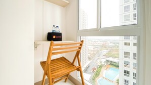 A corner of a room with a wooden chair, a window, and a shelf with water bottles and a black bag. - Best Deal Studio At 23Rd Floor Tokyo Riverside Pik 2 Apartment (Teluknaga)