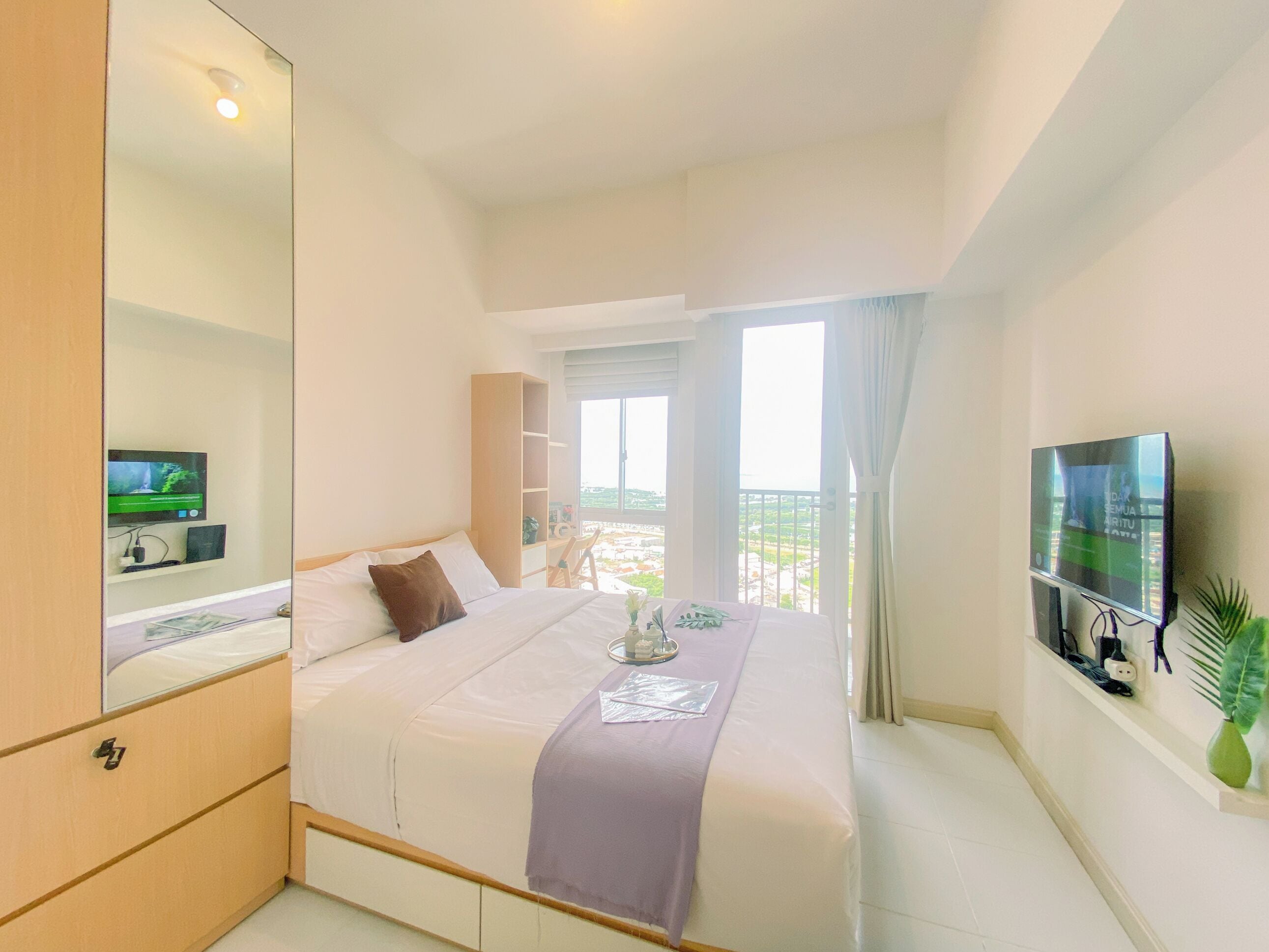 A hotel room with a large bed, a TV mounted on the wall, and a balcony with a view.