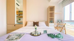 A neatly made bed with a purple bedspread, a magazine, and a decorative tray with candles and a plant.