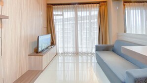 A modern living room with a flat-screen TV on a wooden stand, a sofa, and a large window with sheer curtains. - The Modern Classic 2Br With Scenic View At Gateway Pasteur Apartment (Cimahi)