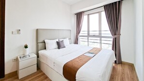 A neatly made bed with a brown accent, a bedside table with a book and a small plant, and a window with curtains. - Cozy And Spacious 1Br At M-Town Signature Apartment (Gading Serpong)