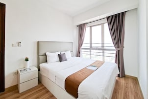 Una cama bien hecha con detalles en marrón, una mesita de noche con un libro y una planta pequeña, y una ventana con cortinas.