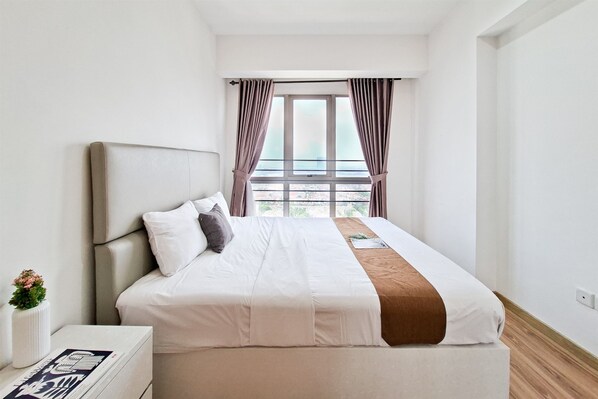 Habitación de hotel moderna con una cama grande, una mesita de noche, una ventana con cortinas y vistas a la ciudad.