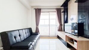 A modern living room with a black leather sofa, a wooden entertainment unit, and a large flat-screen TV. - Cozy And Spacious 1Br At M-Town Signature Apartment (Gading Serpong)