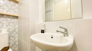 A bathroom with a white sink, a mirror above it, and a toilet with a towel on it.