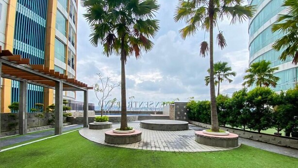 A landscaped courtyard with palm trees, a circular seating area, and modern buildings in the background. - Good Choice Studio Apartment At Sentraland Semarang (Semarang)