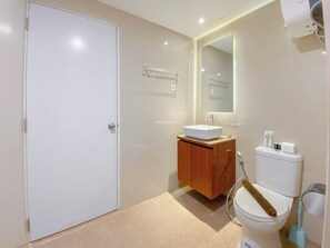 A modern bathroom with a white toilet, a wooden vanity, a white sink, and a mirror above the mirror. - Good Choice Studio Apartment At Sentraland Semarang (Semarang)